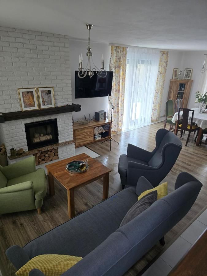Salon z szarą kanapą, fotelami i stolikiem, w głębi jadalnia przy oknie